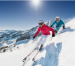 deux skieurs descendent une piste avec vue sur les montagnes derrière eux